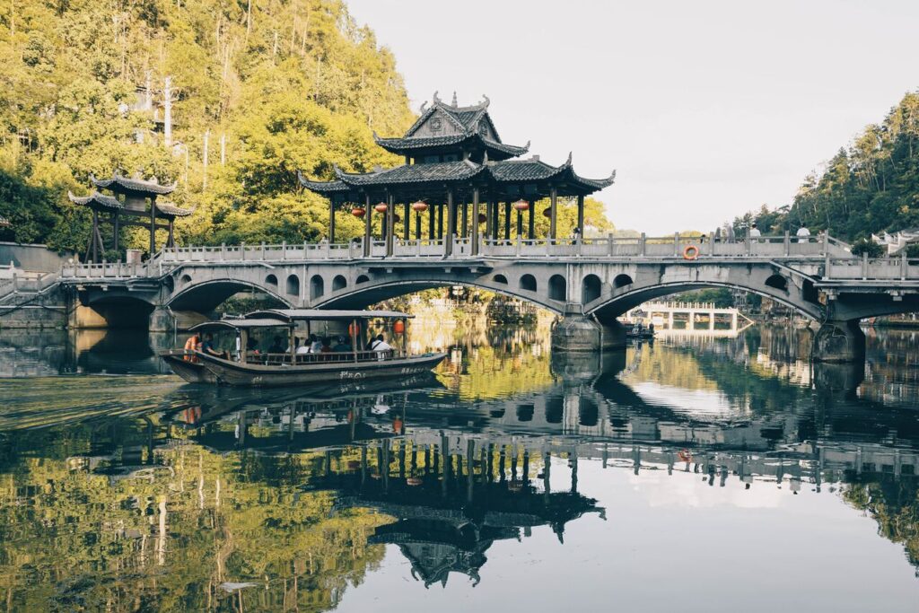 Un barco cruza un río bajo un puente, mostrando la belleza del entorno natural y arquitectónico de China.