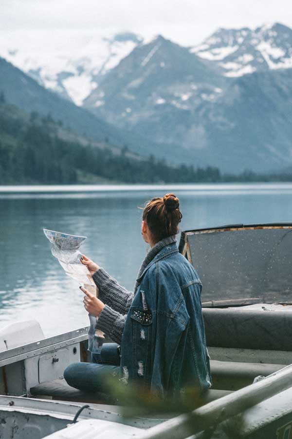 Mujer sobre un barco, leyendo un mapa de fondo unas montañas en china